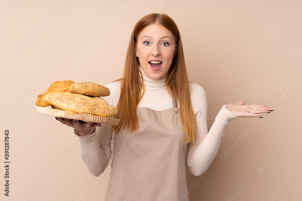 Young redhead woman in chef uniform. Female baker holding a table with several breads with shocked facial expression Young redhead woman in chef uniform. Female baker holding a table with several breads with shocked facial expression
