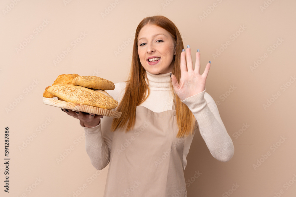 Young redhead woman in chef uniform. Female baker holding a table with several breads saluting with hand with happy expression Young redhead woman in chef uniform. Female baker holding a table with several breads saluting with hand with happy expression