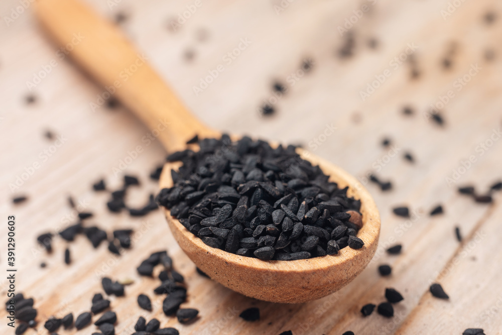 Black cumin seeds on wooden spoon on wooden background Black cumin seeds on wooden spoon on wooden background