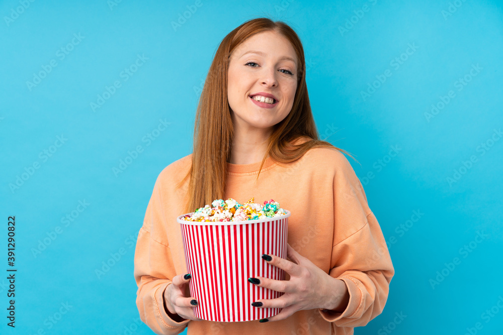 Young redhead woman over isolated background holding a big bucket of popcorns Young redhead woman over isolated background holding a big bucket of popcorns