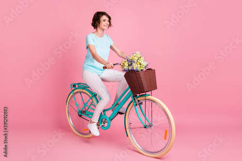 Full length profile photo of sweet cheerful woman wear casual riding teal bike wild flowers isolated pastel pink color background