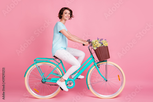 Full length photo of cheerful positive woman wear casual outfit riding bike with wild flowers isolated pastel pink color background © deagreez