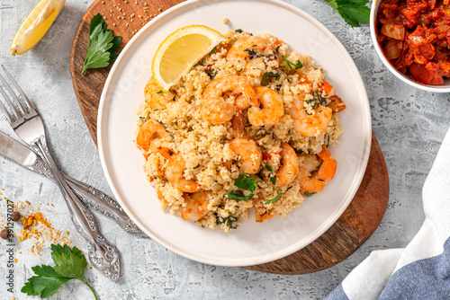 Foto Couscous with fried shrimps, tomatoes, onions, and herbs in a white plate on a gray concrete table top view