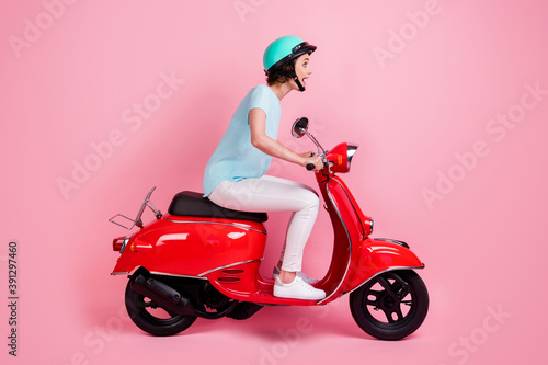 Profile photo of impressed funny young lady ride moped wear white trousers sneakers blue slam t-shirt isolated on pastel pink background