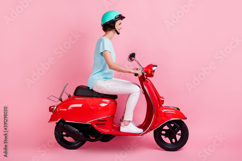 Profile view portrait of pretty glad girl riding red moped wear slam t-shirt trousers shoes isolated on pink color background