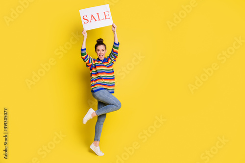 Full length photo of excited young woman hold card word sale raise hands isolated on shine yellow color background