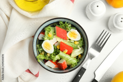 Delicious salad with crab sticks and eggs in bowl on white wooden table, flat lay