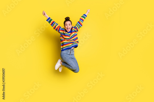 Full body photo of triumphant young woman jump air goal raise hands wear rainbow sweater isolated on yellow color background