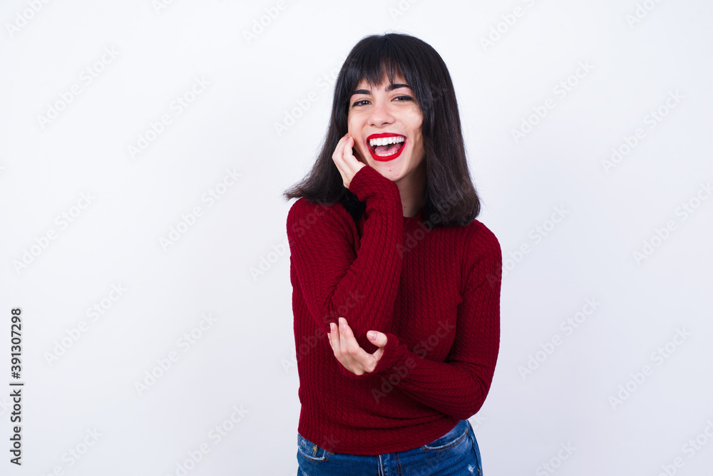 Shocked, astonished Beautiful young Caucasian woman standing against white looking surprised in full disbelief wide open mouth with hand near face. Positive emotion facial expression body language. Shocked, astonished Beautiful young Caucasian woman standing against white looking surprised in full disbelief wide open mouth with hand near face. Positive emotion facial expression body language.