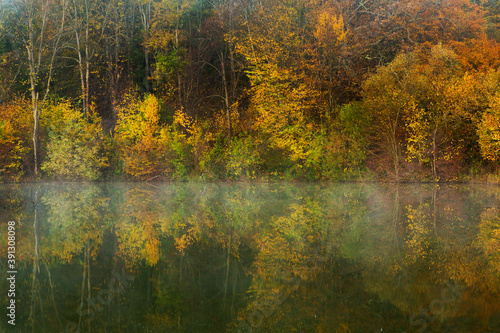 Beautiful landscape with lake and forest. Amazing nature wallpaper. Autumn trees in foggy morning. Romantic place. 