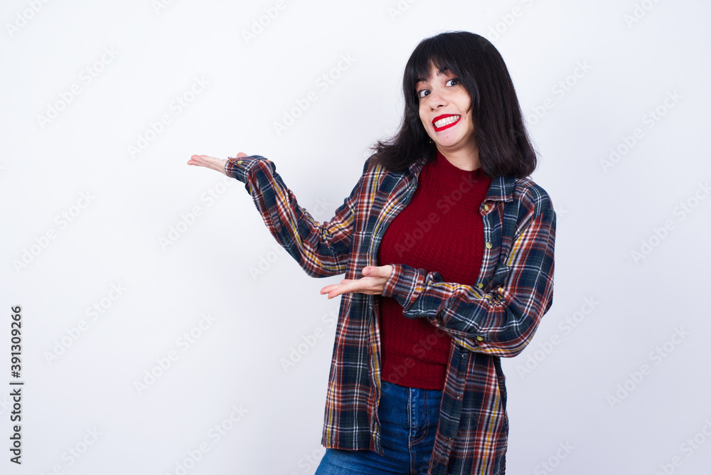 Beautiful young Caucasian woman standing against white background pointing aside with both hands showing something strange and saying: I don't know what is this. Advertisement concept. Beautiful young Caucasian woman standing against white background pointing aside with both hands showing something strange and saying: I don't know what is this. Advertisement concept.