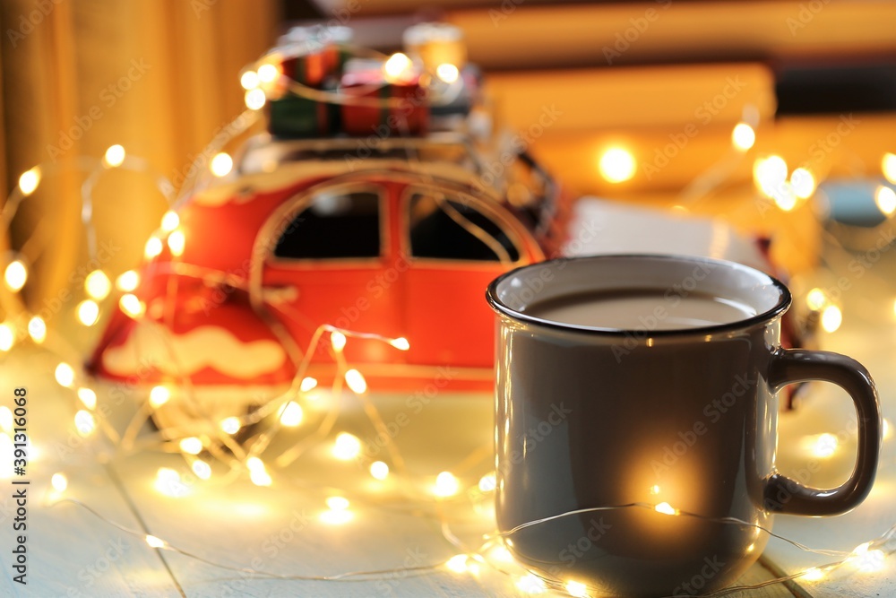 Christmas and New Year festive background.Winter books.Winter cozy reading.A stack of books, a mug of tea, a shining garland and a red decorative car on a light blue wooden background.Winter comfort