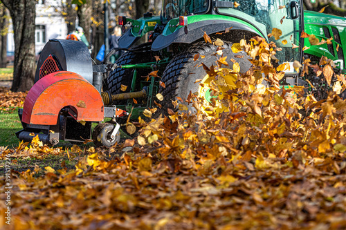 a tractor with a blower cleans a city park lawn and blows away autumn leaves, close-up