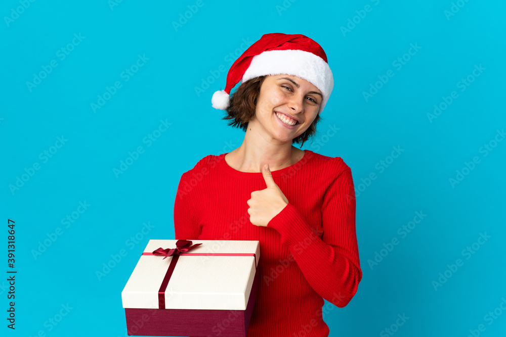 English girl with christmas hat holding a present isolated on blue background giving a thumbs up gesture English girl with christmas hat holding a present isolated on blue background giving a thumbs up gesture