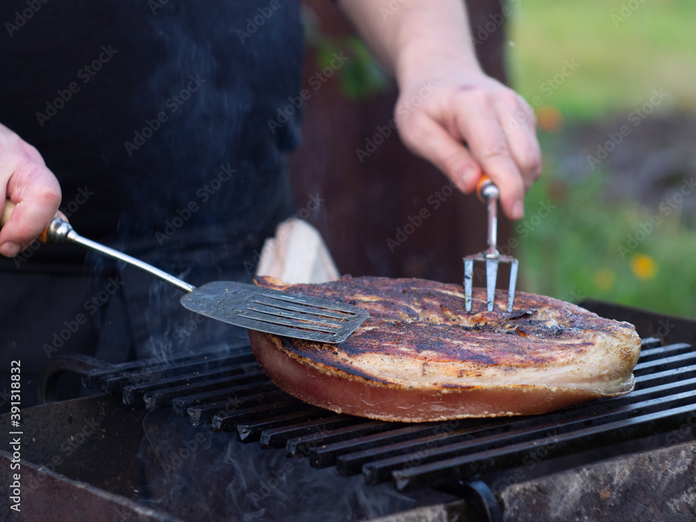 Fototapeta premium a man roasts a large steak on the grill. steak with a pork leg bone.