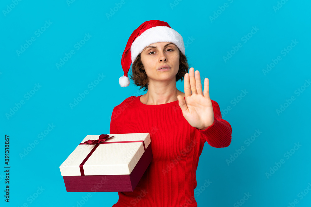 English girl with christmas hat holding a present isolated on blue background making stop gesture English girl with christmas hat holding a present isolated on blue background making stop gesture
