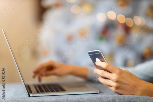Cropped Hands Of Man Using Smart Phone and Laptop Against Christmas Tree 