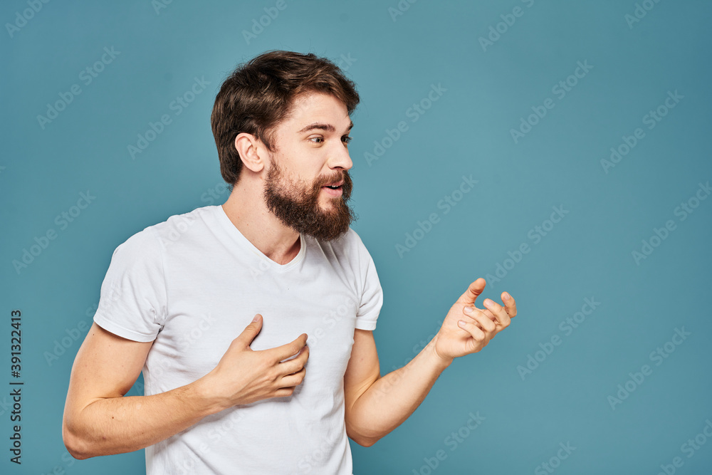 A bearded man in a white T-shirt gestures with his hands emotions blue background A bearded man in a white T-shirt gestures with his hands emotions blue background