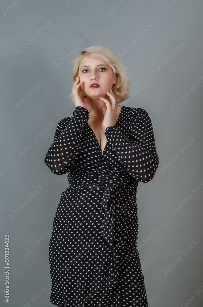 Portrait of a young blonde girl in a dark dress in white polka dots, hands near the face, looking at the camera Portrait of a young blonde girl in a dark dress in white polka dots, hands near the face, looking at the camera