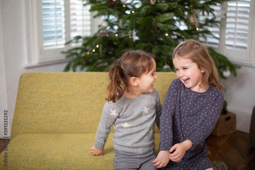 Two young girls sitting on sofa in living room, smiling at each other. Two young girls sitting on sofa in living room, smiling at each other.