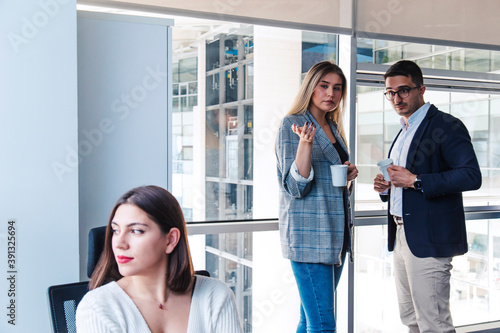 Turkish white collar woman is working on desk and there are two colleagues are gossiping at background behind of her