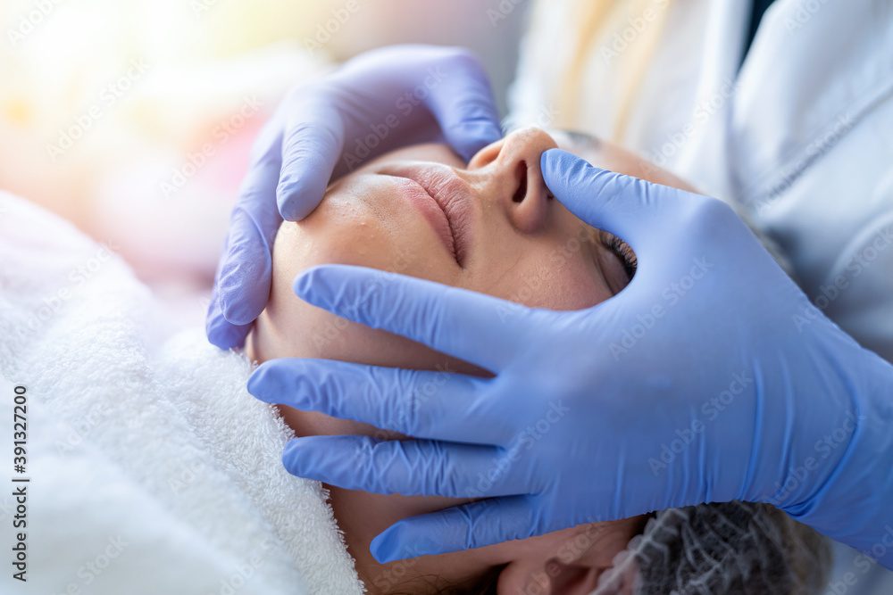 Fototapeta premium Cosmetologist hands in blue gloves touch face of young patient making massage