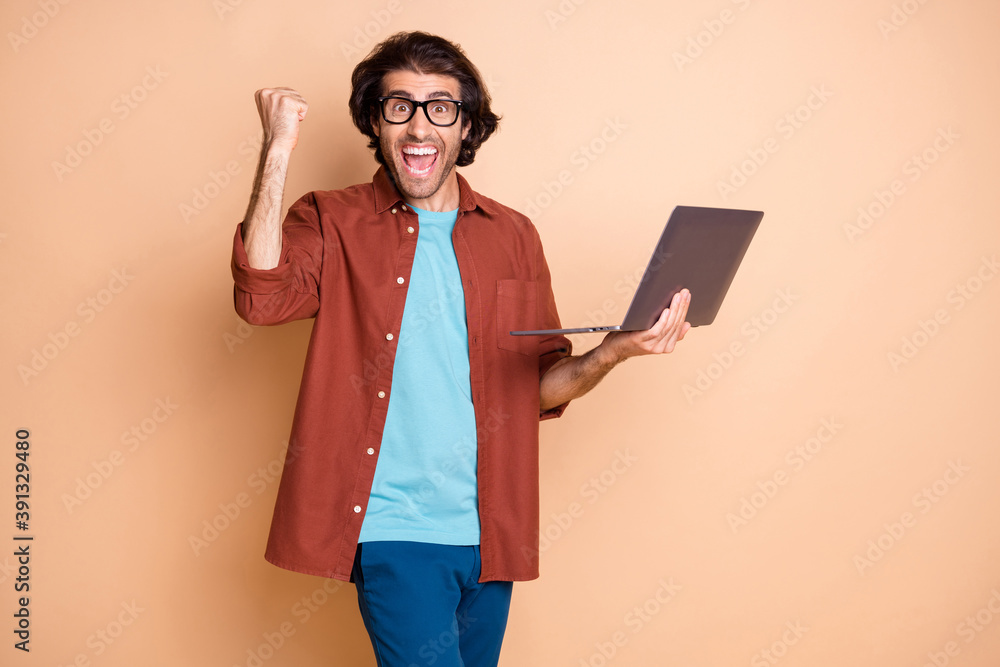 Photo portrait of cheerful guy celebrating holding laptop in hand isolated on pastel beige colored background Photo portrait of cheerful guy celebrating holding laptop in hand isolated on pastel beige colored background
