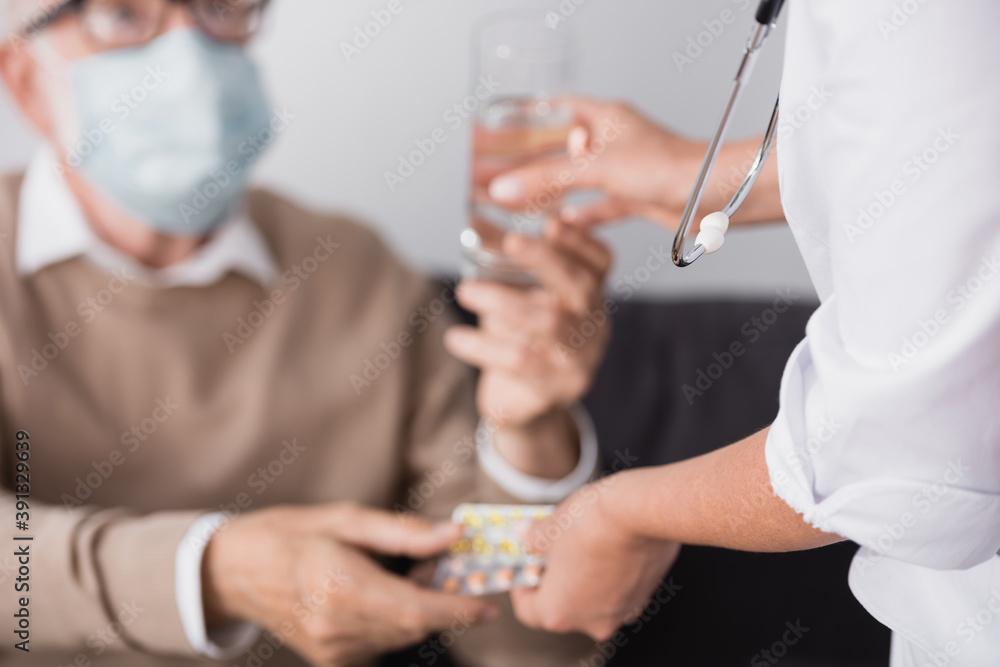 cropped view of social worker giving medicines and water to elderly man on blurred background cropped view of social worker giving medicines and water to elderly man on blurred background