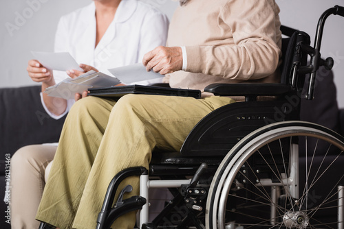 cropped view of social worker showing family photos to handicapped man on blurred background