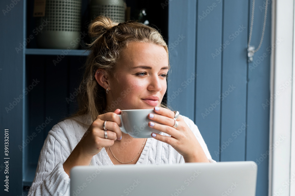 Young blond woman sitting alone at a cafe table with a laptop computer, working remotely. Young blond woman sitting alone at a cafe table with a laptop computer, working remotely.