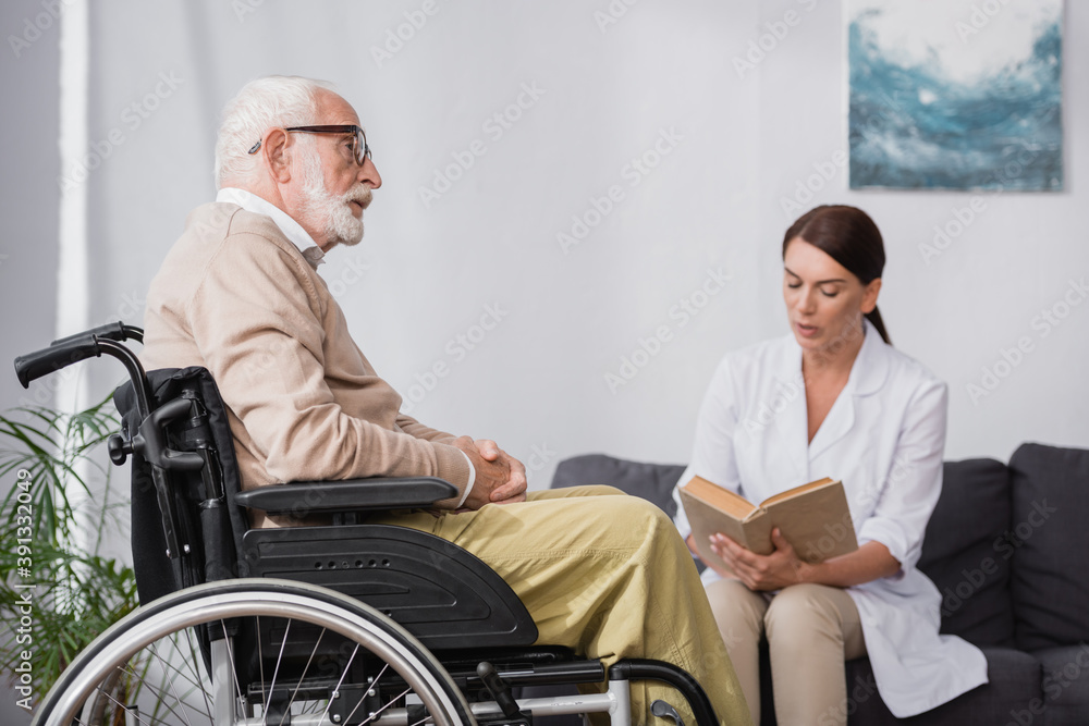 geriatric nurse reading book to aged handicapped man on blurred background geriatric nurse reading book to aged handicapped man on blurred background