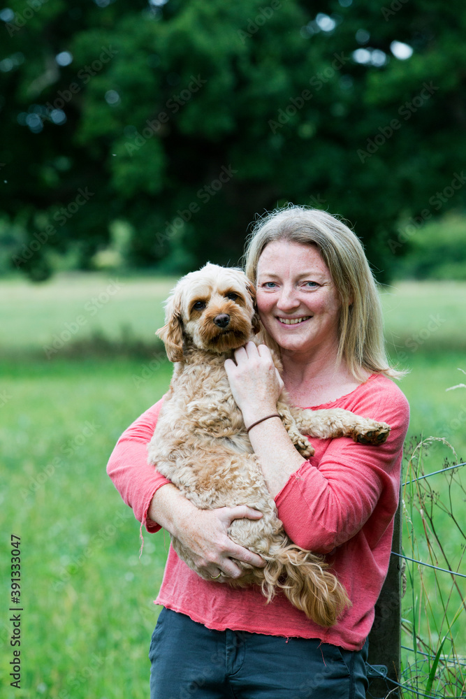 Portrait of smiling woman holding red coated young Cavapoo. Portrait of smiling woman holding red coated young Cavapoo.