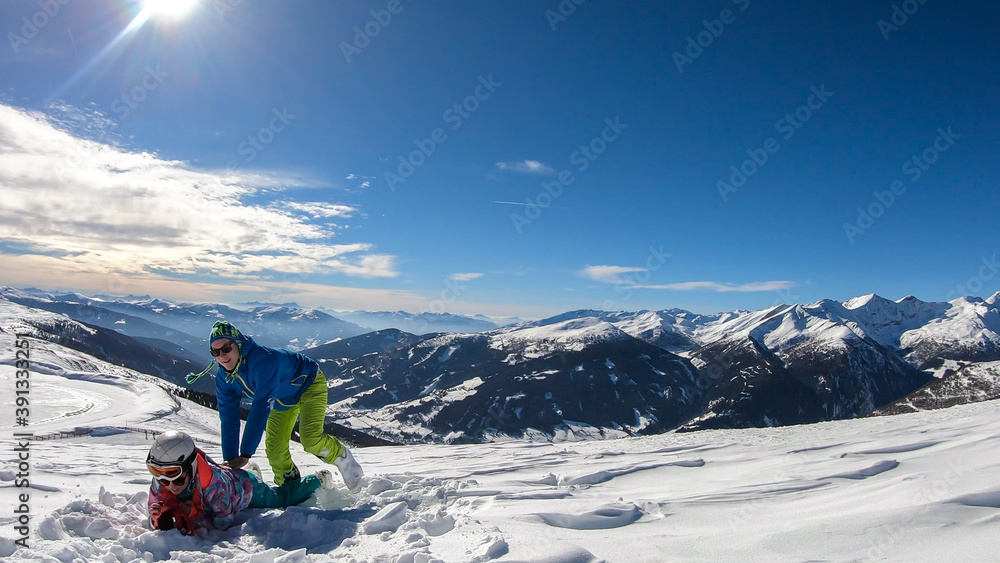 A couple playing in the snow on top of Katschberg in Austria. They are happy and joyful. Panoramic view on the surrounding mountains. Winter wonderland. Bright and sunny winter day. Love and happiness