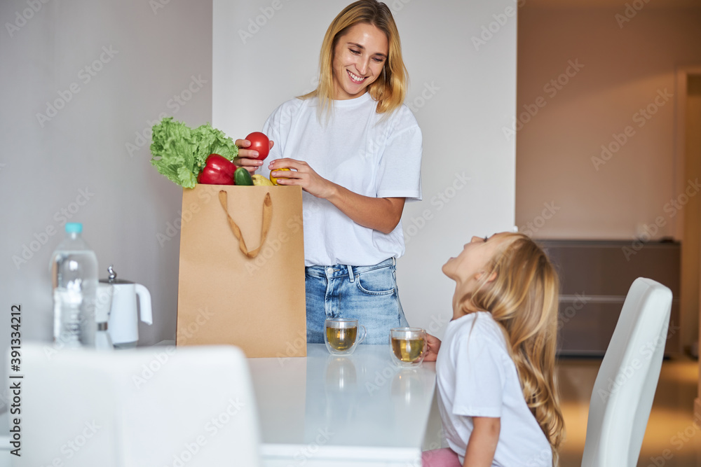 Happy cheerful mother with vegetables in paper shopping bags at home Happy cheerful mother with vegetables in paper shopping bags at home