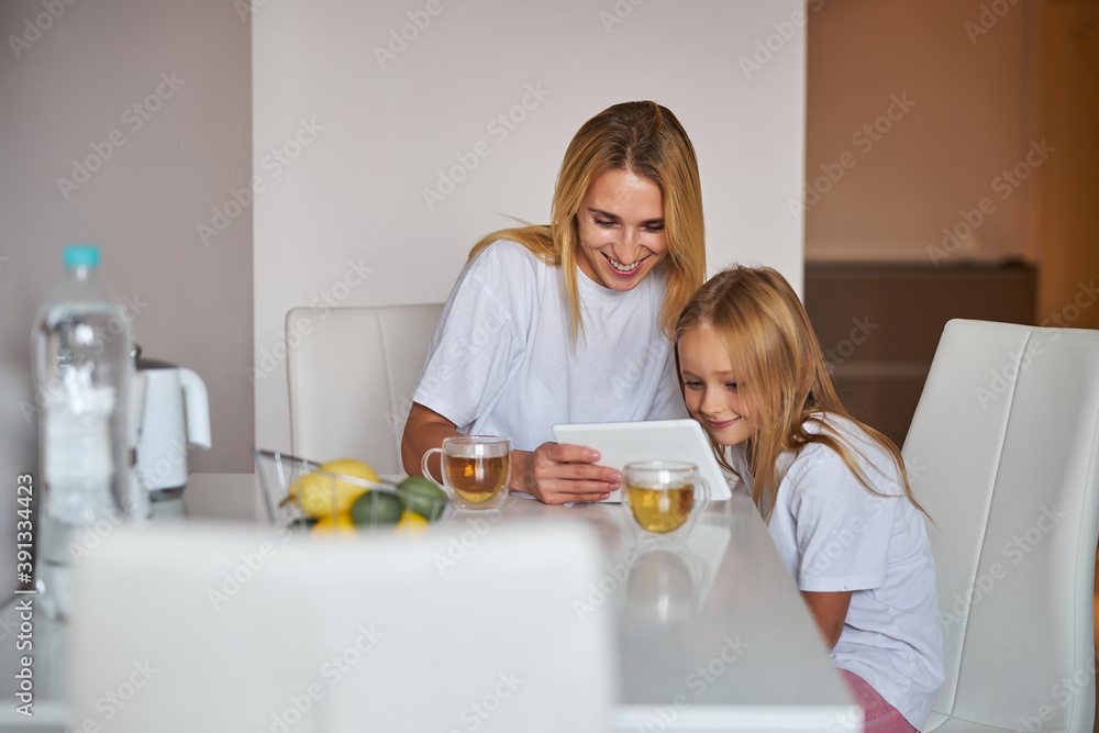 Happy smiling mother with daughter sitting at the white table and having fun together Happy smiling mother with daughter sitting at the white table and having fun together