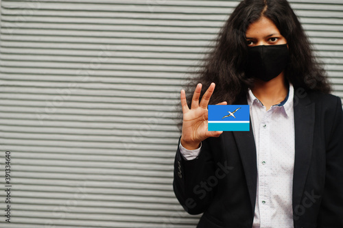 Asian woman at formal wear and black protect face mask hold Midway Atoll flag at hand against gray background. Coronavirus at country concept. photo