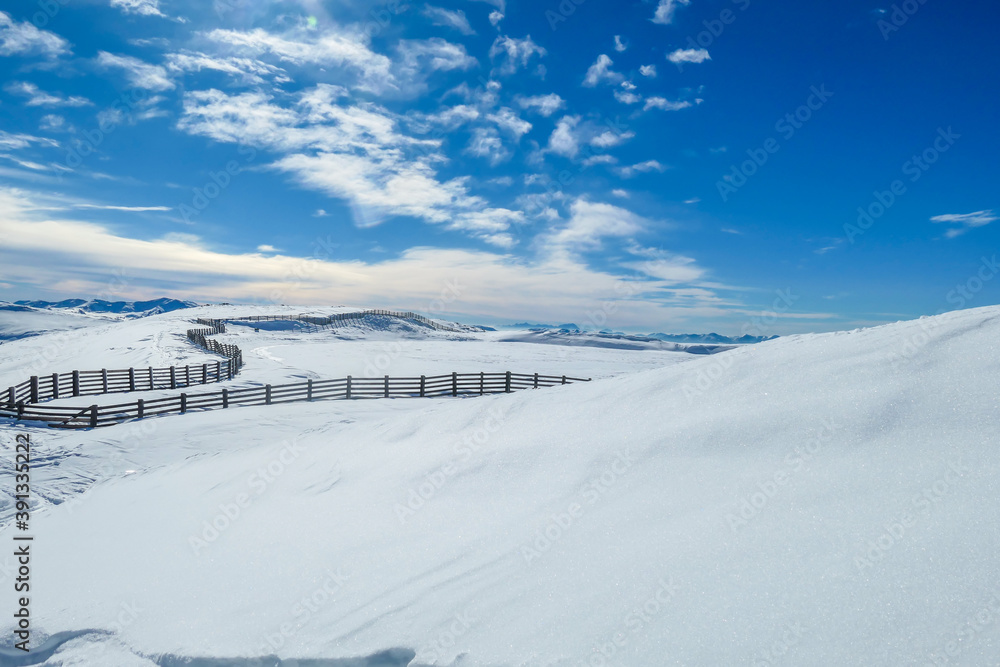 Panoramic view on snow capped Alps in Austria, seen from Katschberg Ski Resort. There is a fence going through the middle of the slope. The slopes are covered with fresh, powder snow. Winter landscape