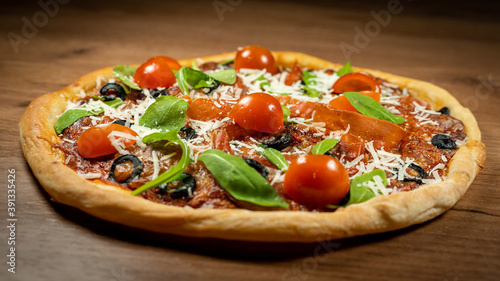 Classic Italian pizza topped with prosciutto, black olives, arugula and cherry tomatoes on rustic wooden surface. Close-up image