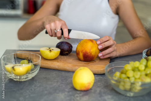 young sporty woman cutting fresh different fruit on wooden table in the kitchen