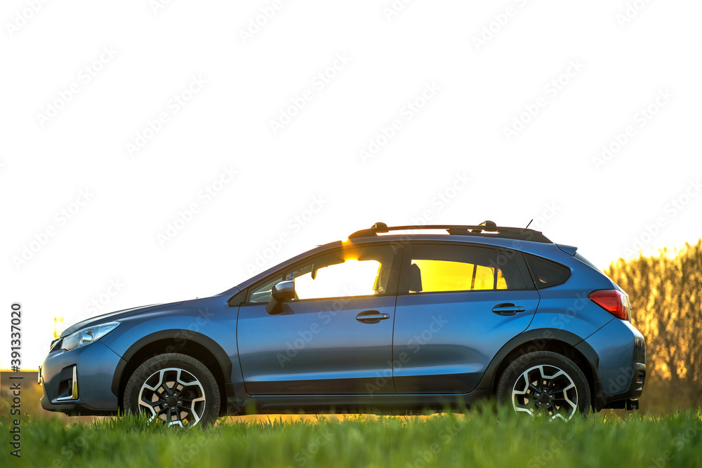 Landscape with blue off road car on green grass at sunset. Traveling by auto, adventure in wildlife, expedition or extreme travel on a SUV automobile. Offroad 4x4 vehicle in field at sunrise.