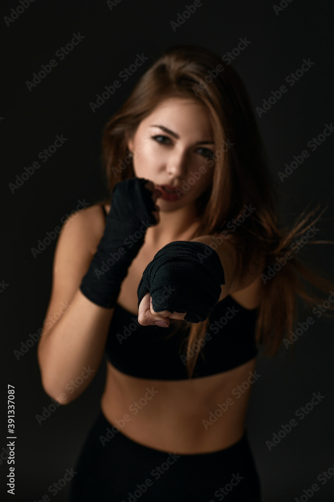 woman with boxing bandages punching on black background. Focus on hand. Woman prepare to trianing session and kickboxing