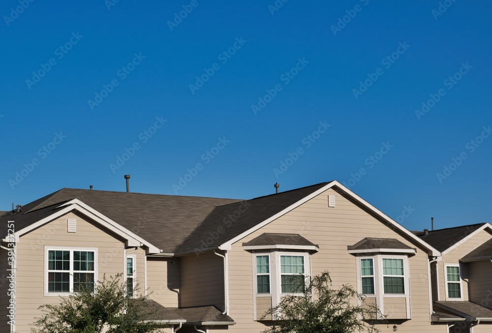 Townhome rooftops in the suburbs in a city subdivision under a clear blue sky with copy space above. Townhome rooftops in the suburbs in a city subdivision under a clear blue sky with copy space above.