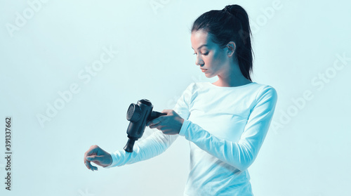 Athletic young female massaging hand by handheld massage gun in neon light, post-workout recovery routines