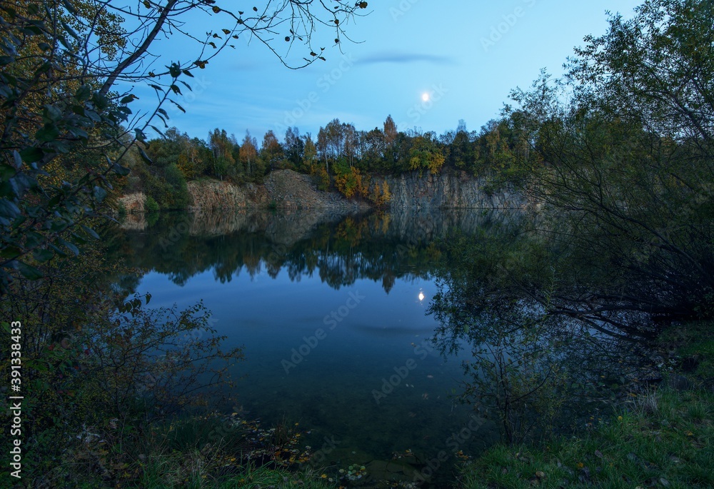 Flooded old quarry in the autumn evening. Moon reflection in water. Czech Republic. Europe. Flooded old quarry in the autumn evening. Moon reflection in water. Czech Republic. Europe.