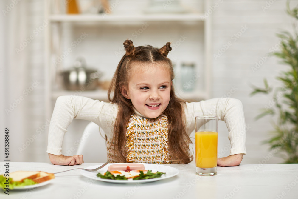 little child girl having breakfast - fried egg and orange juice in the kitchen. healthy breakfast. fried egg face smiles on a white plate little child girl having breakfast - fried egg and orange juice in the kitchen. healthy breakfast. fried egg face smiles on a white plate