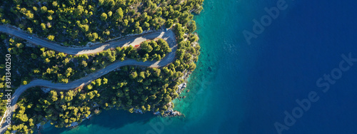 Aerial drone ultra wide top down panoramic photo of curvy snake road crossing through vegetated tropical forest by the sea