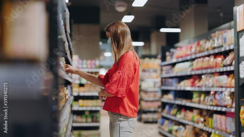 Young woman selecting canned mushrooms showing to her boyfriend consulting searching nutrition together doubting to buy putting back on shelves. Supermarket shopping.