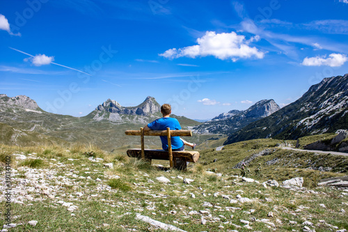 A man sits on a wooden bench against the backdrop of a mountain landscape. Mountain landscape of Durmitor National Park, Montenegro, Europe, Balkans, Dinaric Alps, UNESCO World Heritage Site.