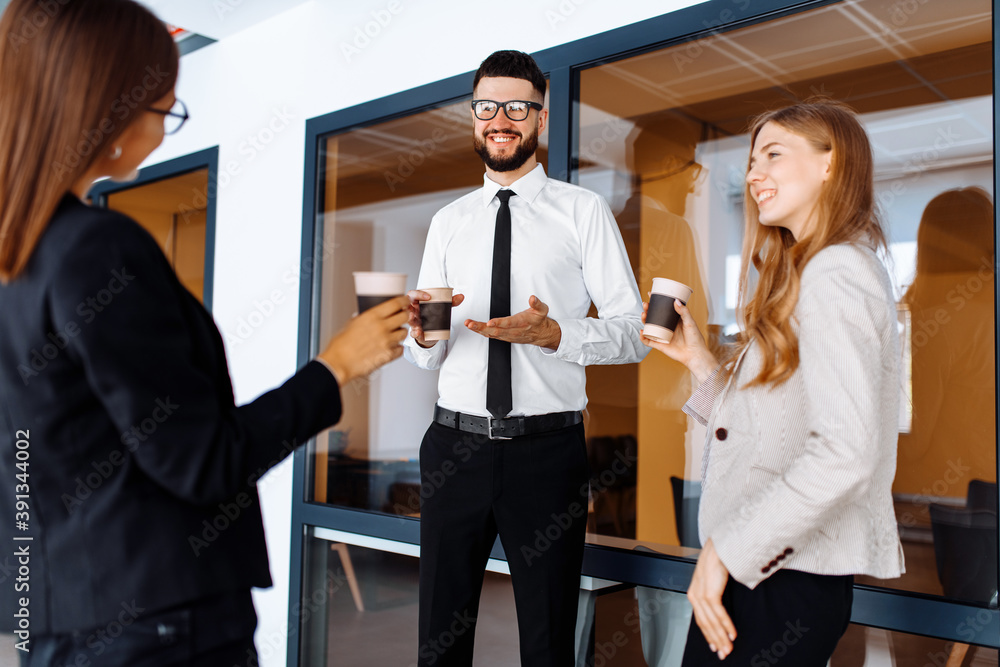 Group of attractive business people standing and communicating together, holding cups, in a modern office. Coffee break. Group of attractive business people standing and communicating together, holding cups, in a modern office. Coffee break.