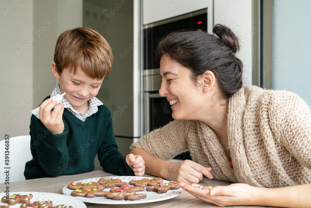 Horizontal view of candid moment of motherhood in the kitchen baking Christmas cookies. Little boy kissing mom with joy doing home made activities at home. Lifestyle with kids indoors. Horizontal view of candid moment of motherhood in the kitchen baking Christmas cookies. Little boy kissing mom with joy doing home made activities at home. Lifestyle with kids indoors.